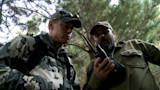 Two hunters in pine forest examining a handheld radio
