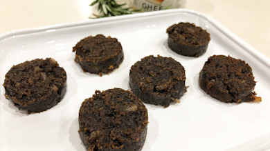 Six round slices of black pudding on a white rectangular plate