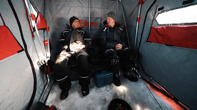 Two anglers sitting inside an Eskimo ice-fishing shelter on snowy ice floor