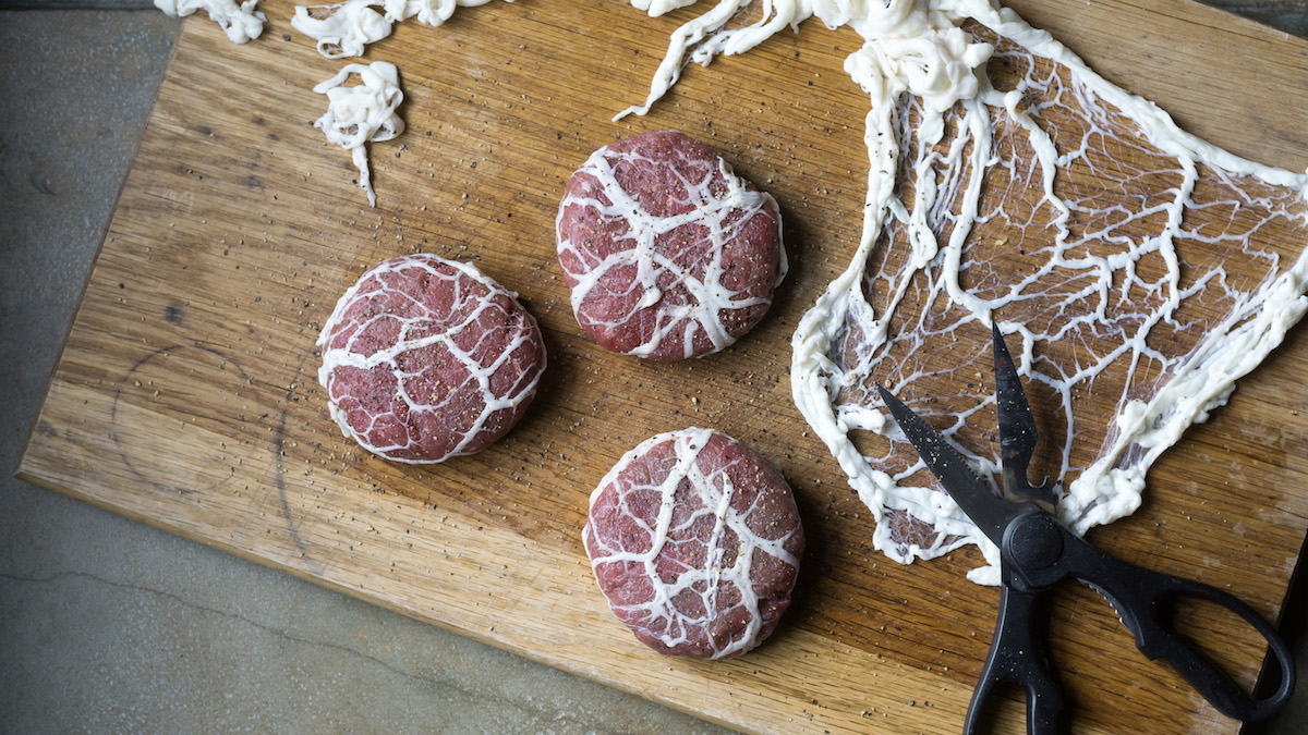 Caul fat burgers on a butcher block ready to cook from Wild + Whole.