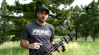 Hunter holding a compound bow in grassy field, wearing t-shirt reading "PRIME"