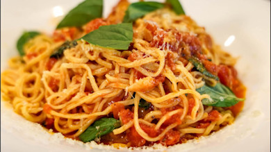 Spaghetti with chunky tomato sauce, basil leaves, and grated cheese on a white plate
