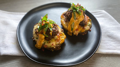 Two loaded twice-baked potatoes topped with shredded meat, melted cheese and scallions on black plate