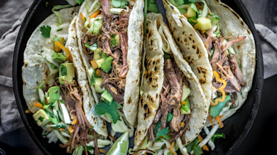 Four shredded-goose tacos with avocado, cabbage slaw, cilantro and lime wedge in skillet