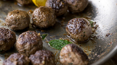 Browned venison meatballs in skillet with mint leaf and lemon wedge