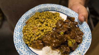 Paper plate of peas and glazed duck over rice held in a hand