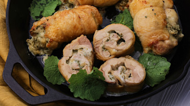 Sliced chicken roulades stuffed with garlic mustard and herbs in cast-iron skillet, garnished with leaves