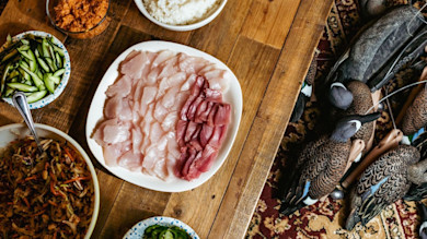 Sliced raw fish on plate with bowls of rice, cucumber, slaw; duck decoys on floor