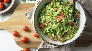 Broccoli tabbouleh with cherry tomatoes in bowl on wooden cutting board