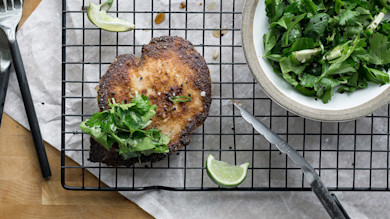 Koji-fried pheasant breast on wire rack with herb salad, lime wedge, knife and fork
