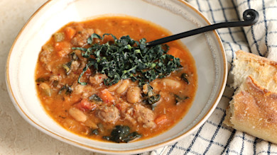 Sausage, bean and kale soup in a bowl with crusty bread and a black spoon