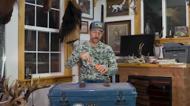 Clay Newcomb using orange knife sharpener at table; YETI cooler and antlers visible