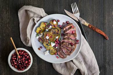 Sliced roasted duck breast with pomegranate seeds and roasted acorn squash on white plate