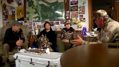 Four people in a hunting cabin talking, man on the right animatedly gesturing