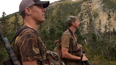 Two hunters with rifles hiking in alpine forest