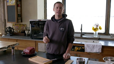Man at kitchen counter preparing raw beef for jerky, cutting board, spice jar, Weston dehydrator