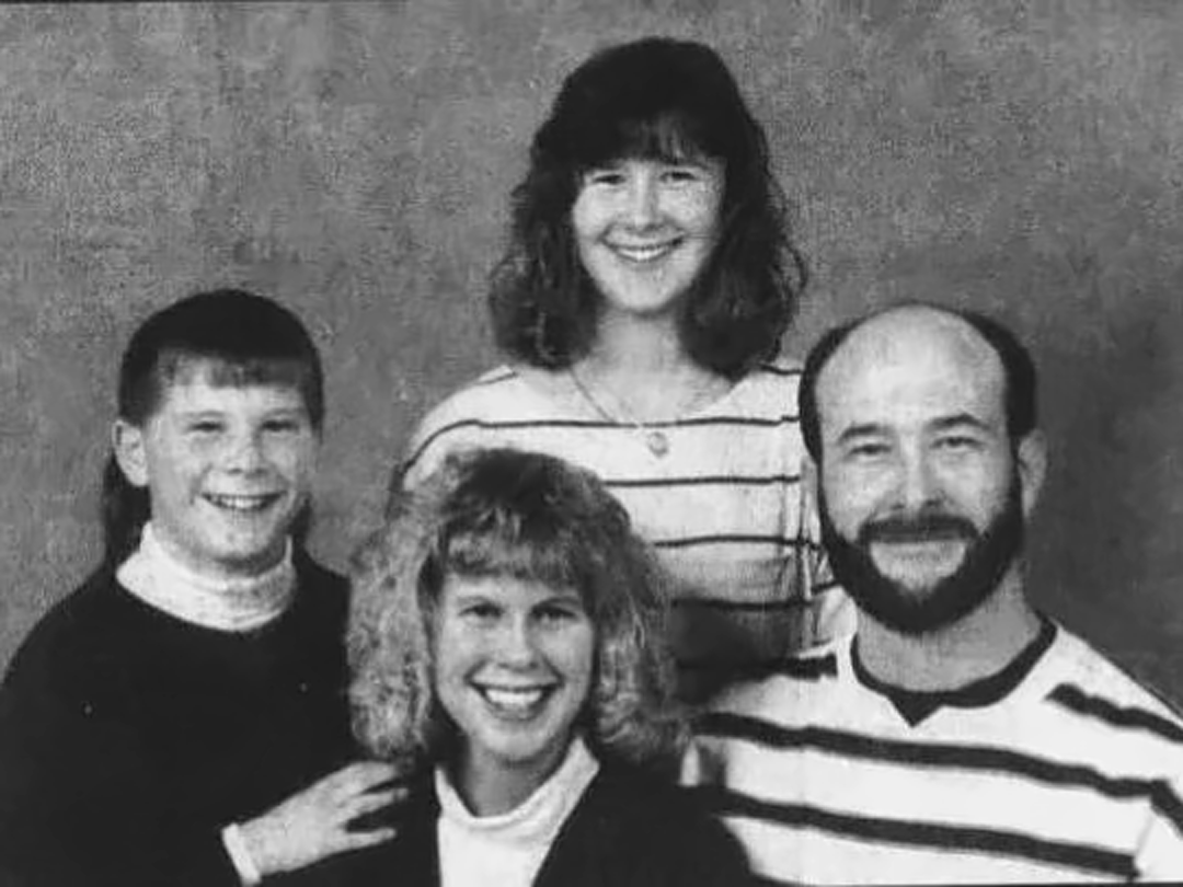 Black-and-white studio portrait of a smiling family: father, mother and two daughters.