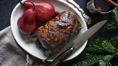 Glazed roast duck on white plate with poached red pears, carving knife and mulled-wine glass