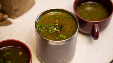 Bone broth in a metal insulated mug garnished with chopped herbs; two red ceramic mugs nearby