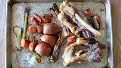 Roasted venison bones with carrots, onions, and celery on a baking sheet