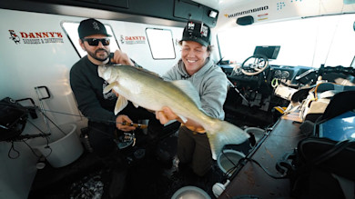 Two men in boat holding a large walleye; visible text: DANNY'S BARBEQUE & SMOKEHOUSE, HUMMINBIRD