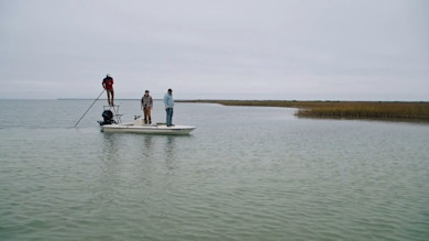Three men fishing from a small skiff in shallow marsh under overcast sky