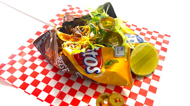 Venison Frito pie in a Fritos bag with shredded cheese, jalapeños, lime on red-check paper