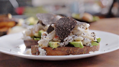 Crab and avocado toast topped with shaved black truffle on a white plate