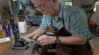 Older man sharpening a knife on a bench jig in a workshop, WD-40 can visible