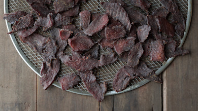 Smoked venison jerky slices on round wire drying rack over wooden table
