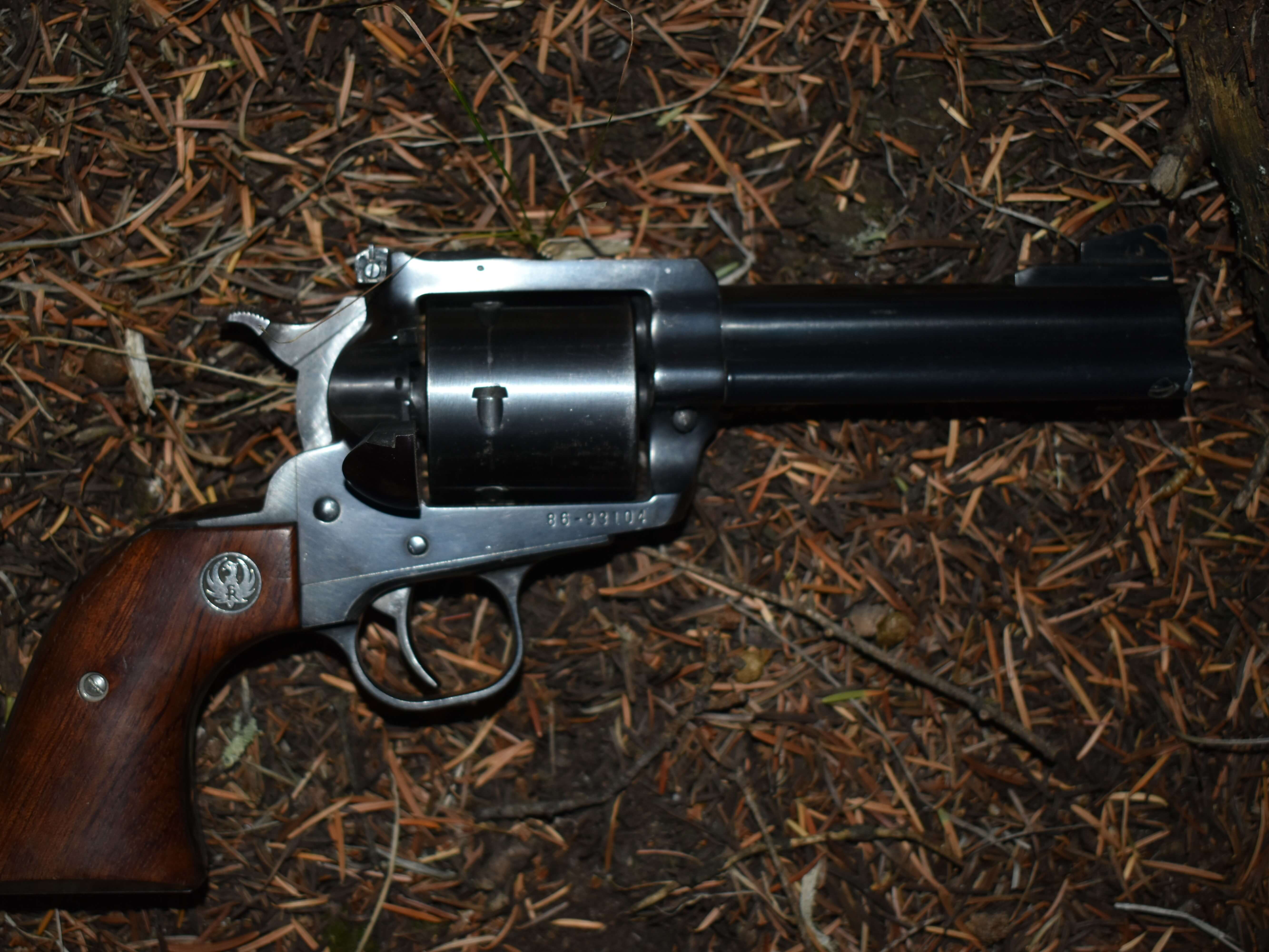 Single-action revolver with wooden grip lying on forest floor among pine needles