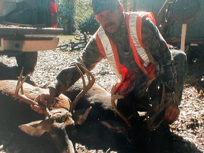 Hunter kneeling in orange safety vest holding antlers of two downed bucks