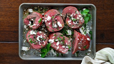 Sliced venison roast stuffed with olives, herbs, and crumbled cheese on metal tray