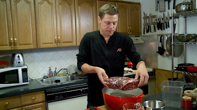Man in kitchen placing raw roast into red Dutch oven
