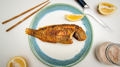 Crispy whole fried fish on blue-rimmed plate with lemon wedges, chopsticks, knife and jar of salt