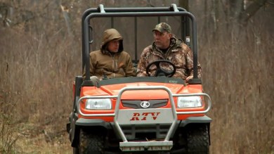 Two hunters in camouflage riding an orange RTV utility vehicle with "RTV" on the front
