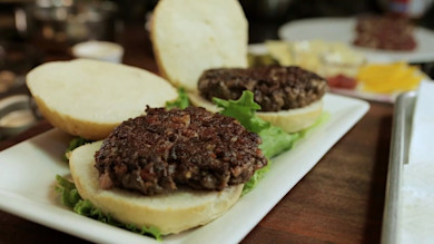 Two open-faced grilled burger patties on buns with lettuce on a white platter