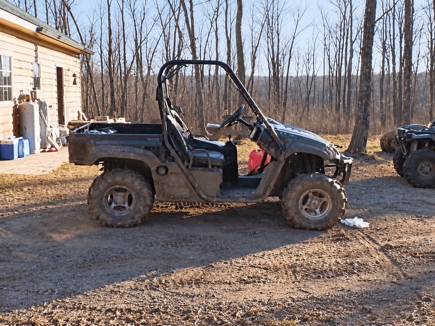Muddy UTV parked beside a wooden cabin, red gas can in the footwell