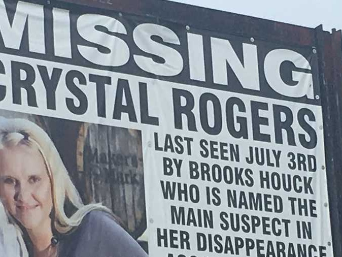Billboard reading MISSING; CRYSTAL ROGERS; LAST SEEN JULY 3RD BY BROOKS HOUCK, with woman's photo