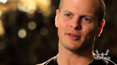 Close-up of man speaking with bokeh lights, overlay text 'MEAT EATER'