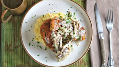 Breaded rabbit schnitzel with creamy mushroom sauce on polenta, garnished with parsley