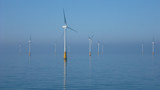 Offshore wind farm with turbines reflected in calm blue sea