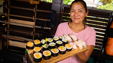 Wooden board of sushi rolls and nigiri held by smiling woman