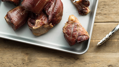 Smoked venison ham hocks on metal baking sheet with tongs on wooden table