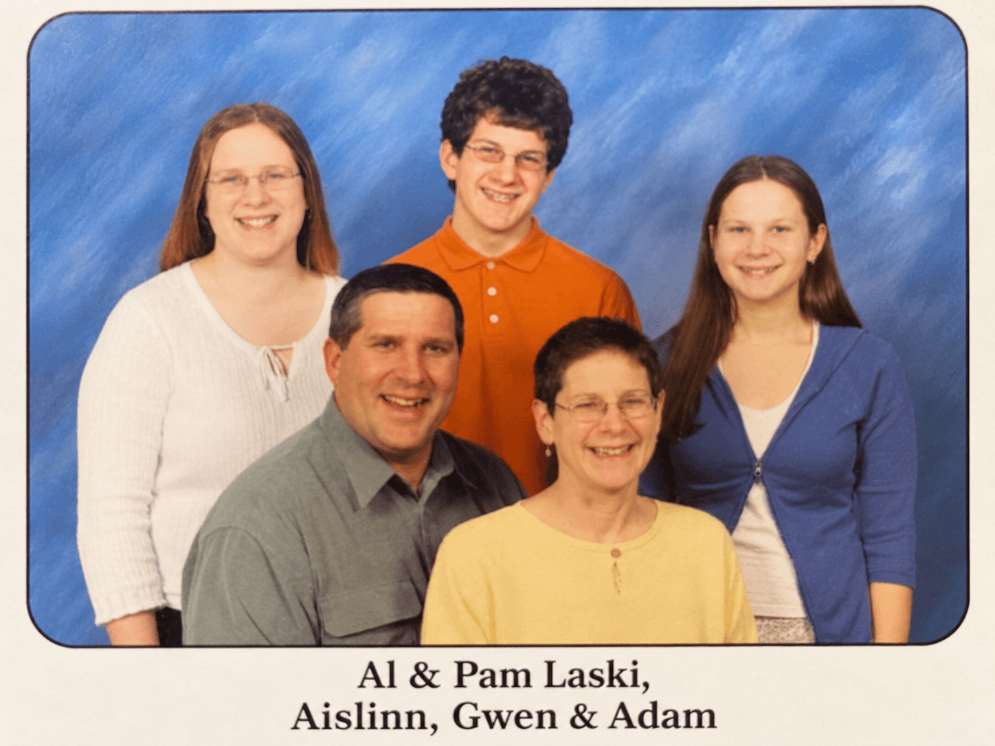 Family portrait, six smiling people against blue backdrop; text: Al & Pam Laski, Aislinn, Gwen & Adam