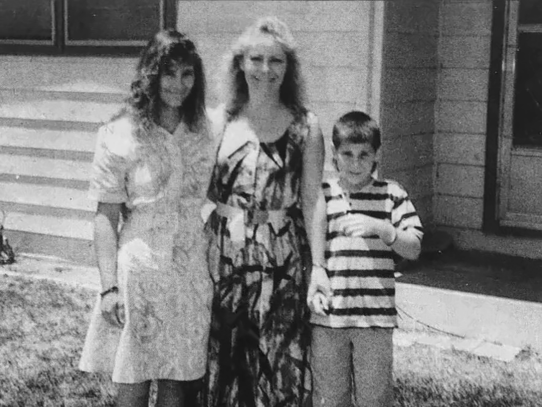 Two women and a young boy standing on a house porch in a black-and-white photo