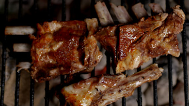 Bone-in venison ribs glazed and searing on a charcoal grill grate