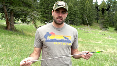 Hunter holding two arrows, wearing T-shirt reading 'HUNT TO EAT' in grassy field