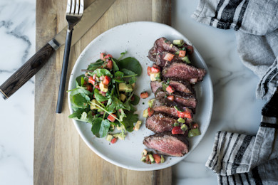 Cocoa-rubbed venison loin, sliced, with arugula salad, avocado and tomato on white plate
