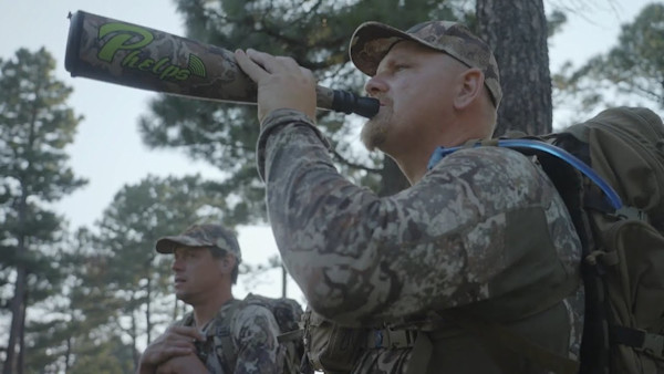 Two hunters in camouflage; foreground man drinking from call labeled Phelps